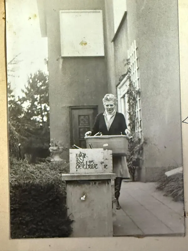 Een vrouw met een bak Oerbier voor een huis